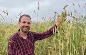Unser Bio-Landwirt Janusz Hradetzky auf dem Getreidefeld kniend neben dem Hafer Sorte Heidegold
