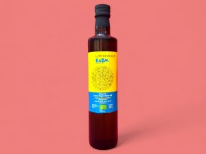 Edem Olivenöl 0,5l, gelbes Etikett mit blauer Schrift Flasche vor rosa Hintergrund
