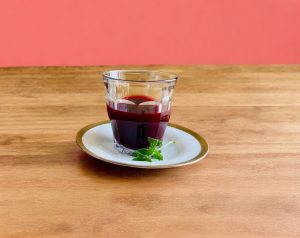 Granatapfelsaft im Glas auf Holztisch vor lachsfarbenem Hintergrund